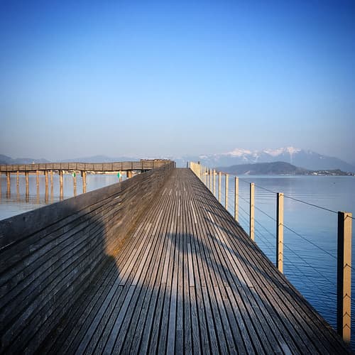 Long wooden pier Holzsteg stretching into tranquil lake Obersee waters, Hurden, Switzerland, March 2019
